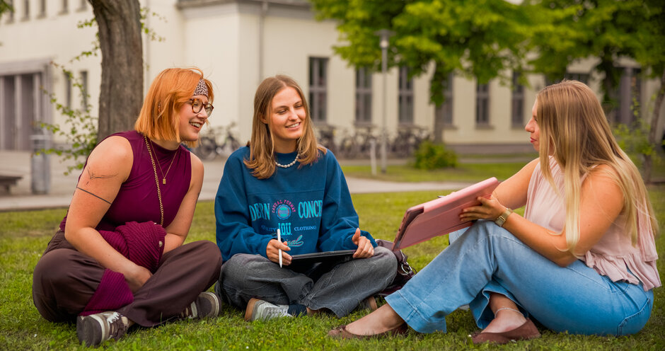 ©FilmVision drei Studierende sitzen auf einer Wiese auf dem Campus der Hochschule Stralsund