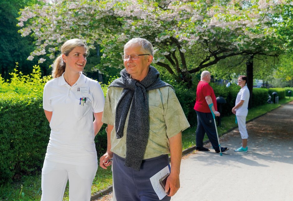 Eine Krankenschwester spaziert mit einem alten Mann durch den Park.