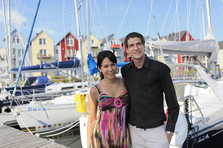 Ein junges Ehepaar steht vor einer Wohnanlage am Museumshafen in Greifswald.
